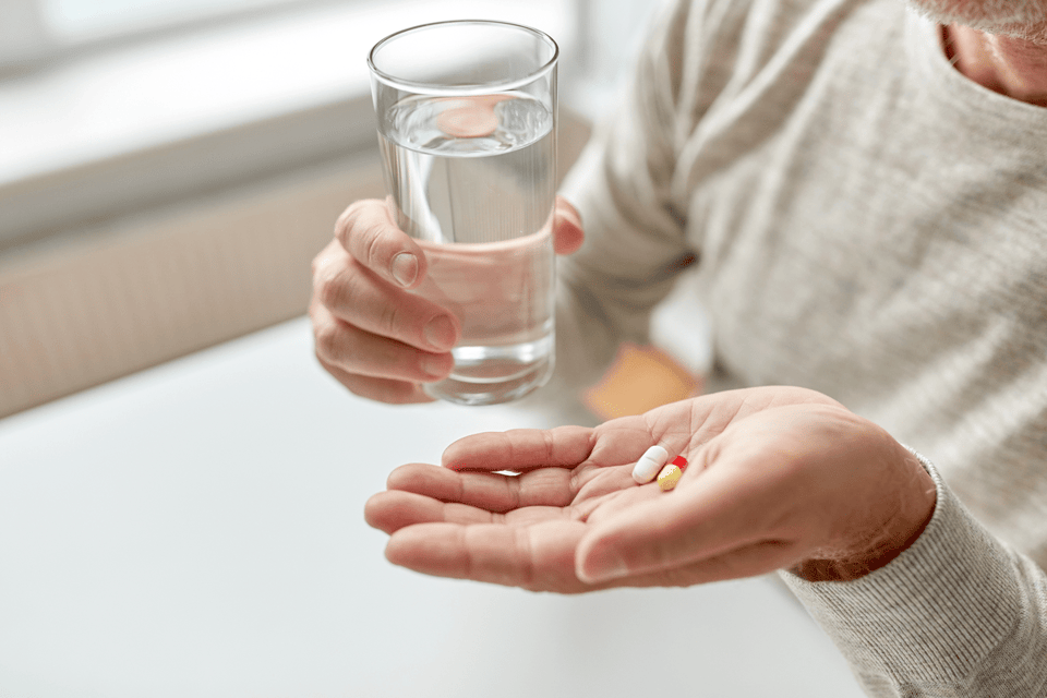 Close up of old man hands with pills and water