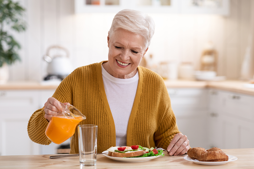 Attractive old lady pouring juice, having lunch in kitchen 